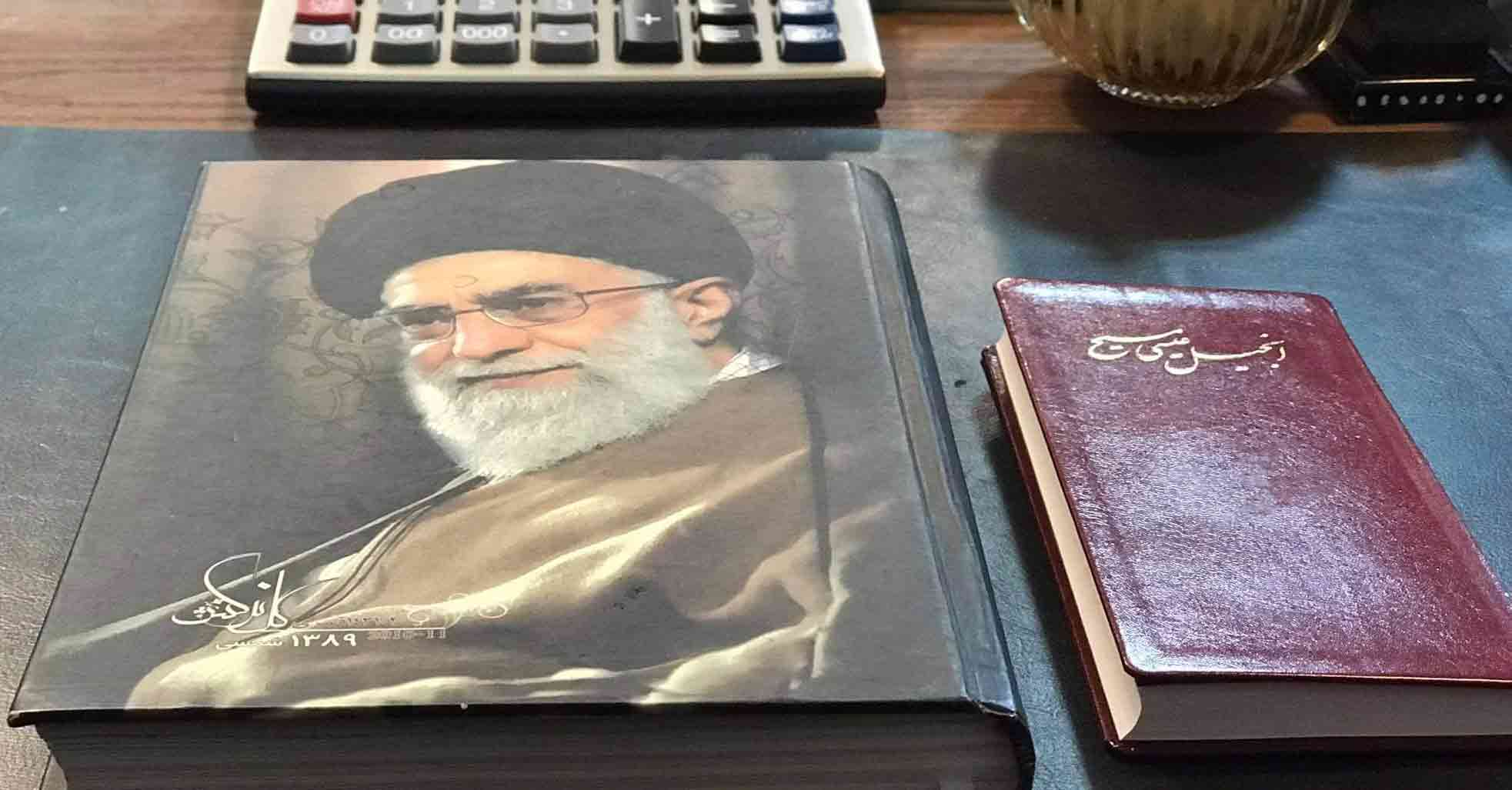 A red New Testament in Farsi next to a portrait of the Iranian ayatollah.